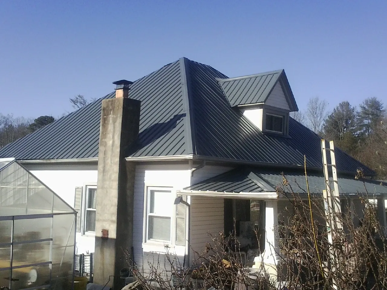 Dark blue standing seam metal roof on a white farmhouse with dormer — Slate & Tile Roof Repair by Roofing Brothers in Hustonville