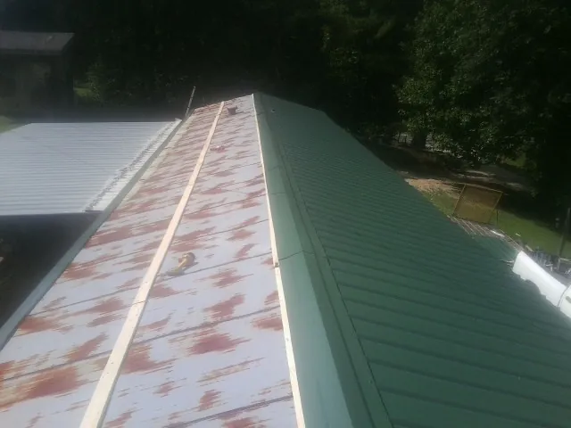 Old rusted panels beside newly installed green metal roofing — Wind Damage Roof Repair by Roofing Brothers in Hustonville