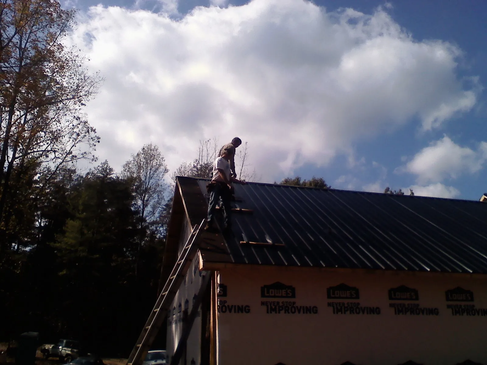 Roofer fastening dark metal panels high against a cloudy sky, from a Roof Inspection job in Hustonville