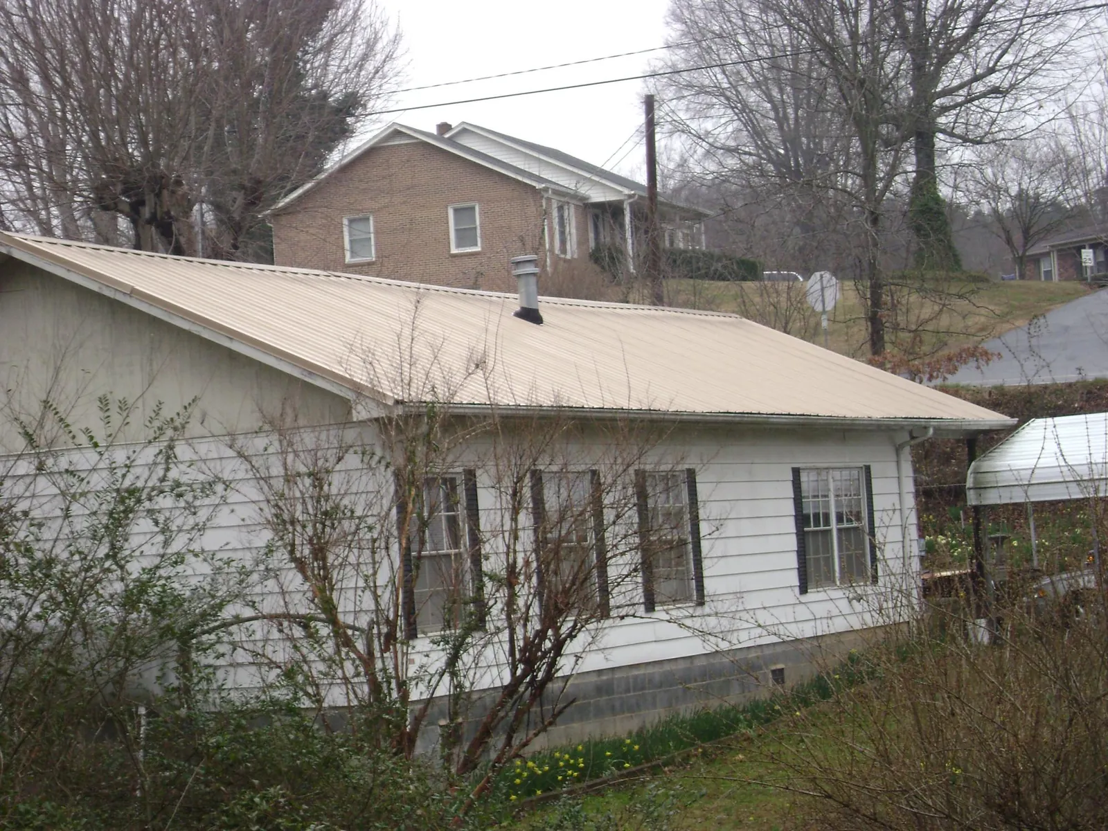 Tan metal roof on a white sided house set into a hillside — Commercial Roofing by Roofing Brothers in Hustonville