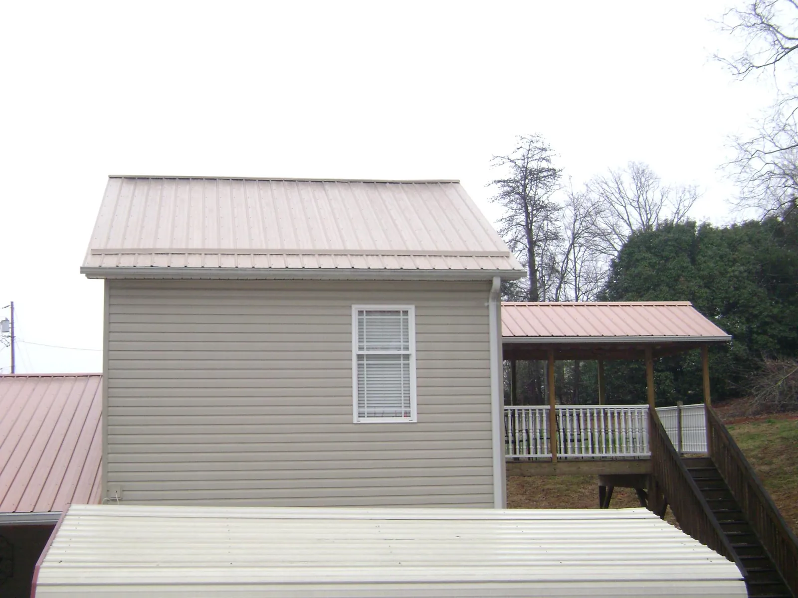 Tan metal roofs on a two story addition and attached porch, from a Roof Replacement job in Hustonville